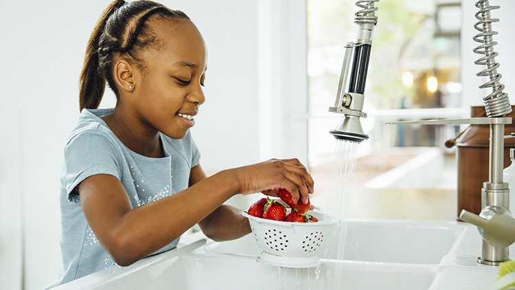 African American girl washing strawberries in kitchen