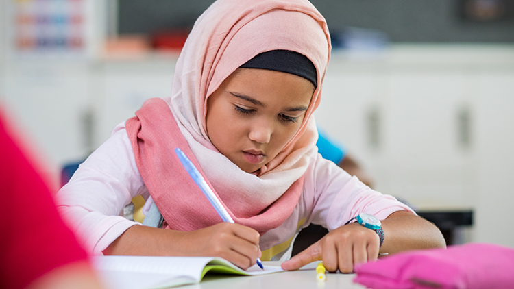 Young girl wearing hijab writing