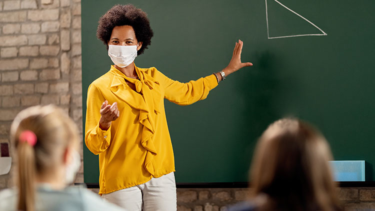 African American elementary school teacher holding mathematics class and wearing protective face mask due to coronavirus pandemic.
