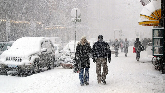 People walking down sidewalks in a snowstorm in a city.