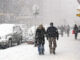 People walking down sidewalks in a snowstorm in a city.